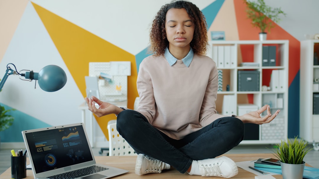 Young African American girl is sitting in lotus pose on office table enjoying relaxation and meditation. Job, stress management and break at work concept. — Foto: Vitaly Gariev / Unsplash