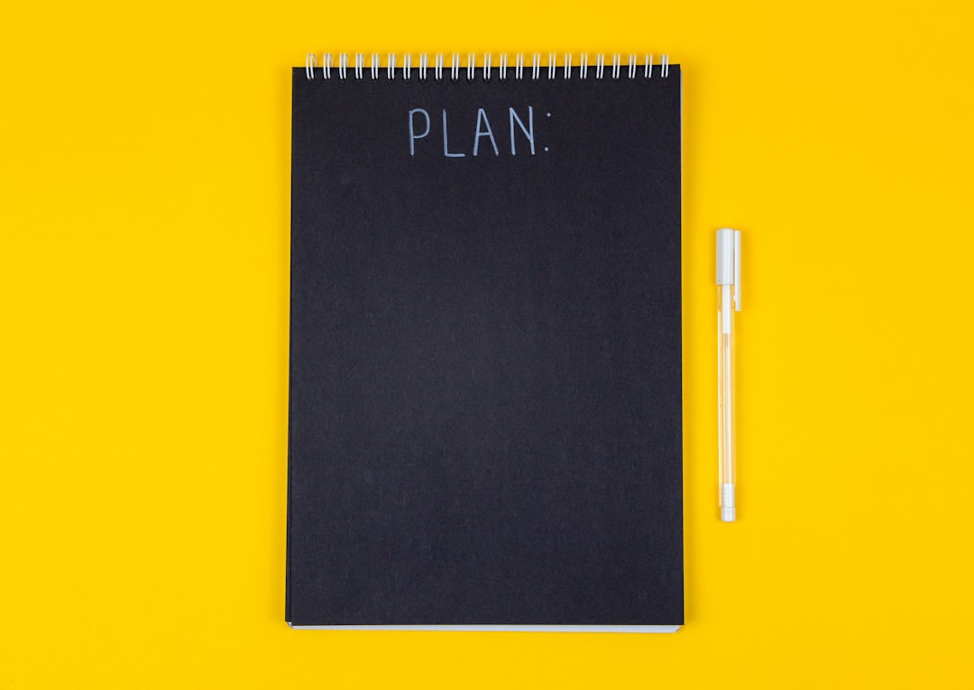 Wide view image of blank black spiral note pad and white marker with calligraphic inscription plan on yellow background — Foto: Volodymyr Hryshchenko / Unsplash
