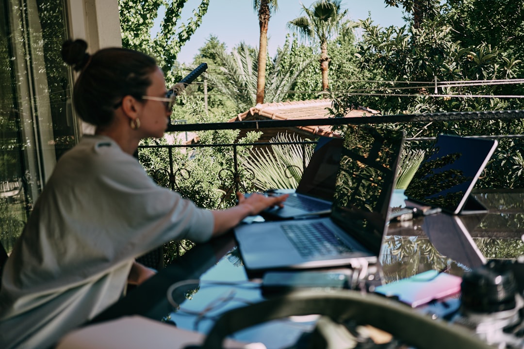 A girl working on the table on the terrace. Many laptops and other staff. Side view — Foto: Aleh Tsikhanau / Unsplash